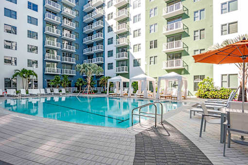 North Miami Beach, FL, Luxury Apartments Near North Beach - Lazul - Swimming Pool Surrounded By Lounge Chairs, Umbrellas, Cabanas, Trees, And A View Of The Apartments.