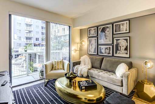 Pet-Friendly Luxury Apartments in North Miami Beach, FL - Lazul - Living Room with Porcelain Wood-Style Plank Flooring, Area Rug, Couch, Armchair, Coffee Table, Side Table with Lamp, Standing Lamp, and Sliding Glass Door with Access to Balcony.