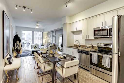 North Miami Beach, FL, Luxury Apartments Near Aventura Mall - Lazul - Kitchen With Soft-Close Cabinetry, Quartz Countertops, Stainless Steel Appliances, Dining Table, Chairs, And Cushioned Bench.