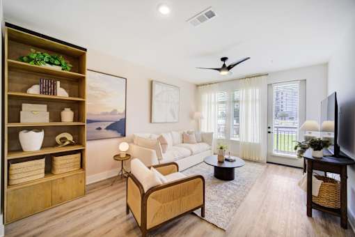 Apartments in Panama City Beach, FL, with In-Unit Washer and Dryer - Vintage Lake Powell - Living Room With Built-In Wood Shelving, White Sofa, Coffee Table, Ceiling Fan, And Large Windows.