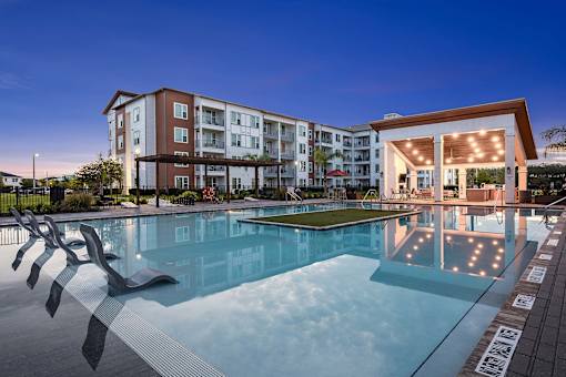 A large swimming pool in front of a building with a sun lounger.