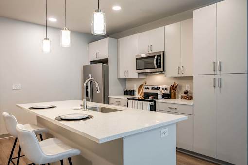 A kitchen with a white countertop and white chairs.