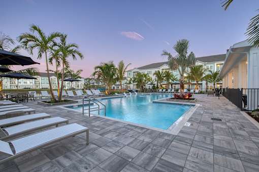 A pool surrounded by palm trees and lounge chairs.