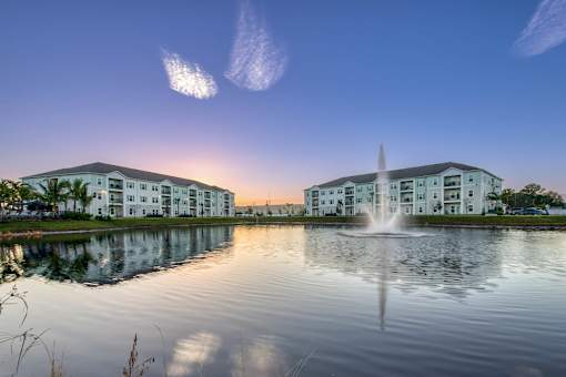 A building with a fountain in front of it is reflected in the water.