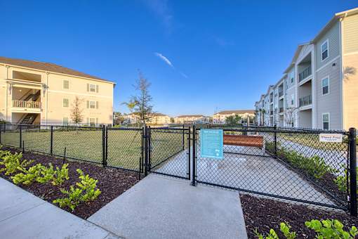 A fenced area with a sign and a bench in front of apartment buildings.