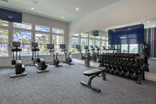 A gym with a row of treadmills, elliptical machines, and a bench press.