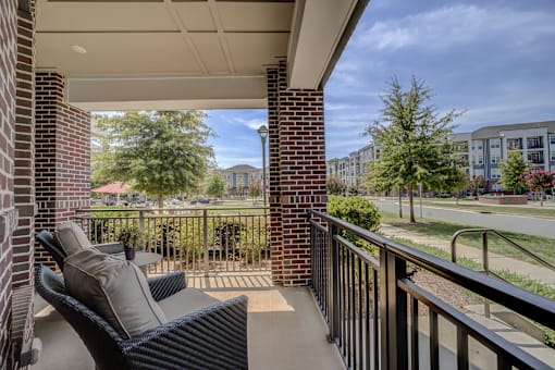 A balcony with a black chair and pillow is overlooking a green lawn.