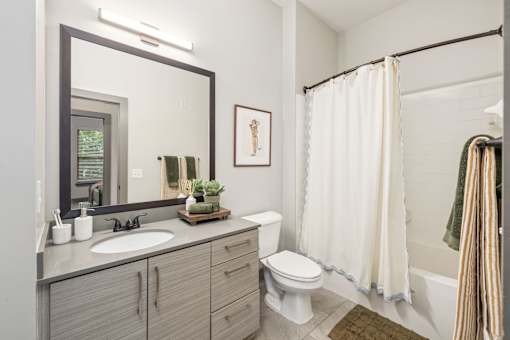 Duluth, GA, Apartments near Stone Mountain Park - District at Duluth - A Bathroom with Shower and Bathtub Combo, Tile Flooring, and Vanity with a Mirror.