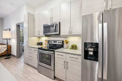 1 Bedroom Apartments in Duluth, GA - District at Duluth - Kitchen with Hardwood-Style Flooring, Quartz Countertops, Stainless Steel Appliances, and White Tile Backsplash.