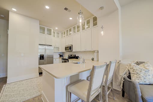 A kitchen with white cabinets and a large island with chairs around it.