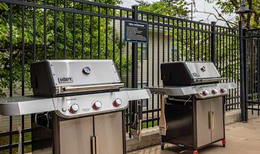 Two grills are placed next to a fence.
