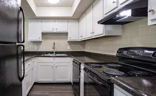 A black refrigerator is in a kitchen with white cabinets.
