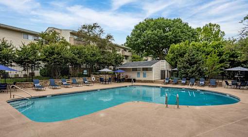 A swimming pool surrounded by chairs and trees.