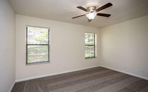 A room with a ceiling fan and two windows.