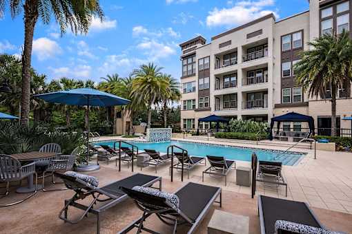 A pool area with lounge chairs and umbrellas in front of a multi-story building.