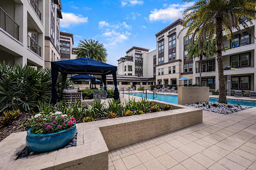 A pool area with a blue canopy and a large planter with pink flowers.
