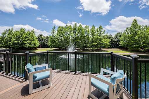 Two chairs on a deck overlooking a lake.