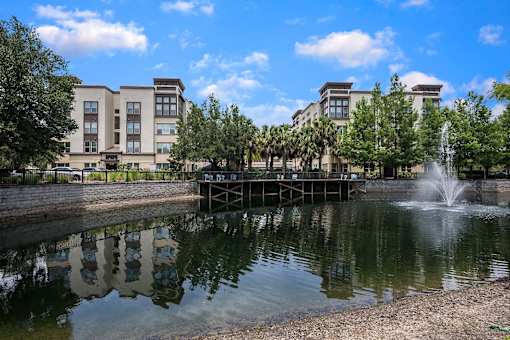 A fountain in the middle of a pond in front of a building.