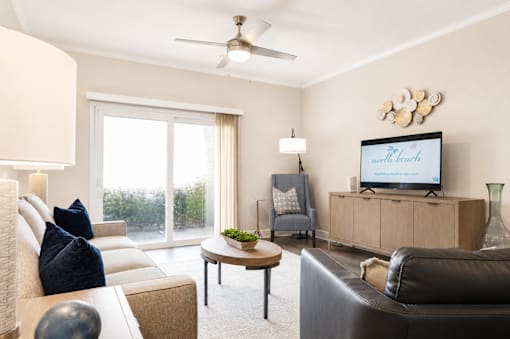 A living room with a couch, a chair, a coffee table, and a television displaying the text "The North Beach".