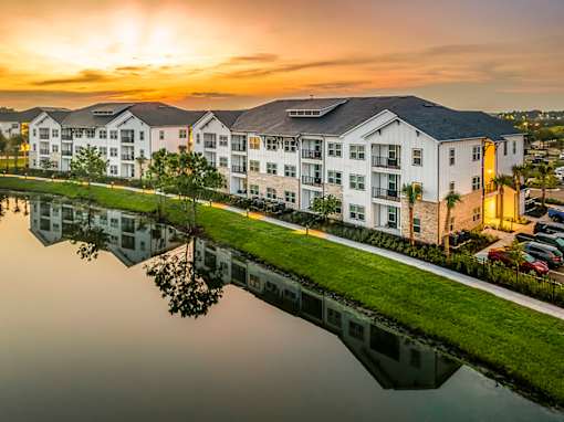A sunset view of a white apartment complex reflected in a body of water.