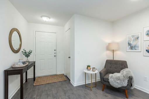 A grey chair with a white fur throw is in front of a lamp and a painting on the wall.
