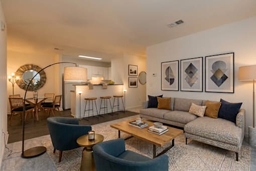 A living room with a grey couch, a blue armchair, a wooden coffee table, and a round mirror.