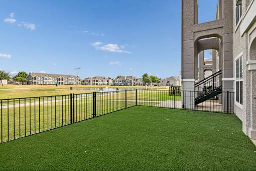 A black fence surrounds a green lawn in front of a building.