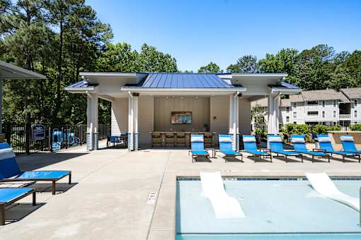 A pool pavilion with a blue roof and white walls is surrounded by blue lounge chairs.