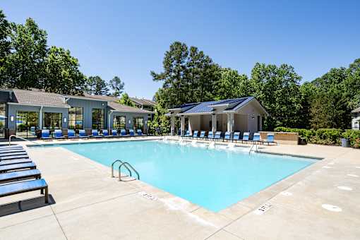 A large swimming pool with sun loungers and a building in the background.