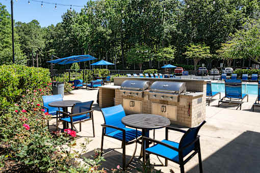A patio with blue chairs and tables is surrounded by greenery.