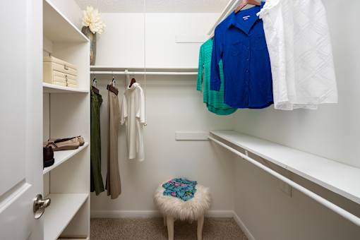 A white closet with clothes hanging and a stool in front.