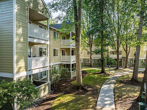 Apartment complex with green trees and a walkway.