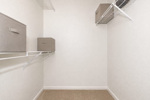 A room with a carpeted floor, a white wall, and a metal shelf with two storage boxes.