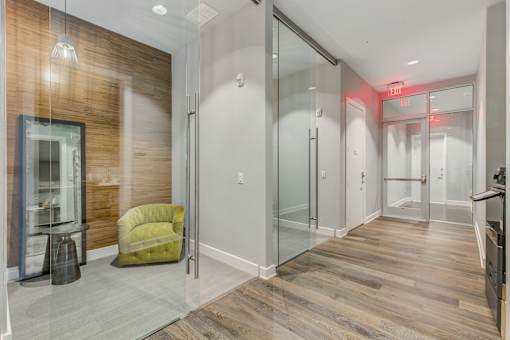 A hallway with a green chair and a glass door.