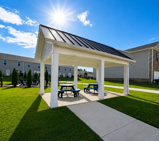 A pavilion with a white roof and blue benches is situated in a grassy area.