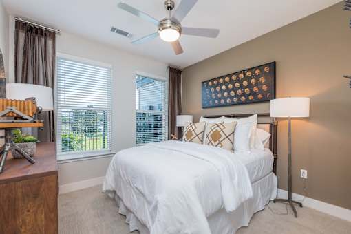 A bedroom with a bed, a ceiling fan, and a window with blinds.