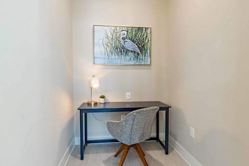 A painting of a bird is hanging on the wall above a desk with a chair and a lamp.