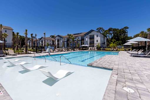 A large swimming pool with sun loungers and a building in the background.