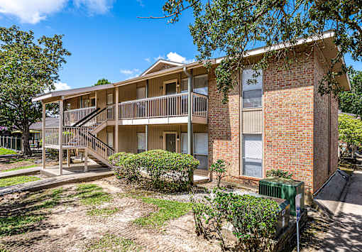 A two-story brick apartment building with a balcony and a small garden in front.
