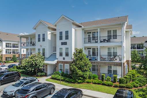 A large white apartment building with a parking lot in front.