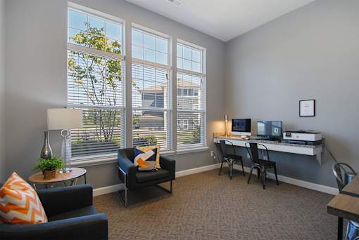 A room with a desk, chairs, and a couch with a window in the background.