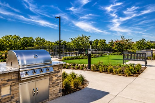 A BBQ grill is on a patio with a fence and trees in the background.