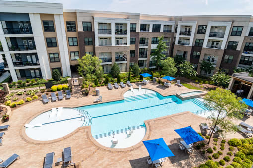 Luxury Apartments in Decatur, GA - Reserve Decatur - Saltwater Swimming Pool with In-Pool and Poolside Lounge Seats, Tables and Chairs with Umbrellas, Trees, and Manicured Shrubs.