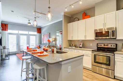 1-Bedroom Luxury Apartments in Decatur, GA - Reserve Decatur - Kitchen with Stainless Steel Energy Star Appliances, Kitchen Island/Breakfast Bar with Barstools, Pendant Lights, Quartz Countertops, White Cabinets, and Subway Tile Backsplash.