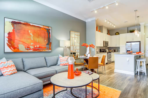 Two-Bedroom Luxury Apartments in Decatur, GA - Reserve Decatur - Open Layout Living Room with Designer Plank Flooring, Area Rug, Sectional Couch, Coffee Table, Wall Art, Standing Lamp, and View of Dining Area and Kitchen.