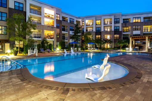 a swimming pool at night with an apartment building in the background