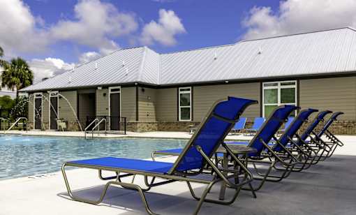 A row of blue lawn chairs are lined up by a pool.
