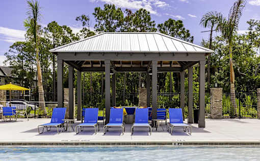 A gazebo with blue chairs is surrounded by a pool.