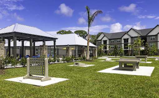 A gazebo is surrounded by benches and trees in a grassy area.