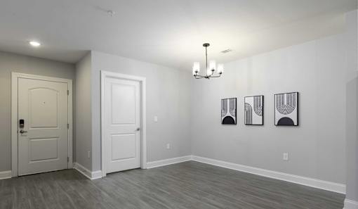 A room with a white door, a white wall, and a chandelier.